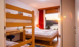 A cozy room with a bunk bed and a double bed. Through the window, there is a view of the landscape at sunset.