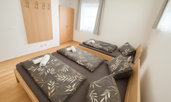 A simple room with four beds, equipped with pillows and blankets. There is a bright atmosphere and hardwood floor, as well as a wardrobe on the wall.