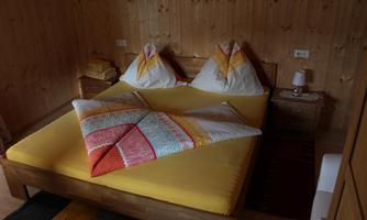 A cozy bedroom with a large bed and colorful cushions. The walls are made of wood and there is a bedside lamp.