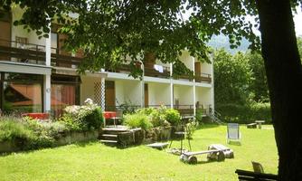 An apartment building with balconies amidst a green meadow. Surrounded by trees and blooming plants, it offers a tranquil atmosphere.