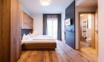 A modern hotel room with wooden furniture and two single beds. The room has large windows and access to the bathroom.