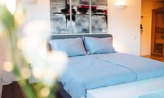 A modern bedroom with a large bed and soft blue bedding. An abstract artwork hangs on the wall, stylishly complementing the space.