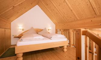A cozy bedroom with wooden walls and wooden furniture. The bed is simple and inviting, perfect for a relaxing stay.