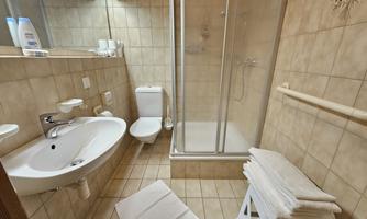 A modern bathroom with a shower and toilet. Clean towels are neatly stacked and the walls are tiled with bright tiles.