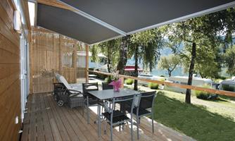 A cozy terrace with a table and chairs, surrounded by trees. In the background, a picturesque landscape with water is visible.