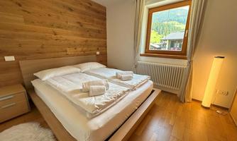 A cozy bedroom with a large double bed and wooden paneling. A window offers a view of the green landscape outside.