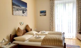 A cozy bedroom with a double bed and large windows. The walls are painted in warm colors and several pictures adorn the room.