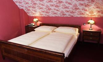 A cozy bedroom with a double bed and two bedside tables. The walls are decorated in a soft pink with a classic pattern.