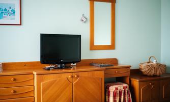 A simple bedroom with a wooden wardrobe, a television, and a mirror. On the table lies a small decorative bag.