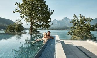 A tranquil infinity pool with a view of a picturesque mountain landscape. Two people are enjoying the water and the nature around them.
