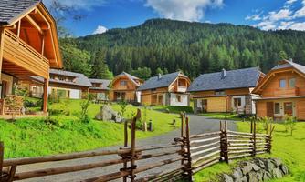 A group of wooden houses in a picturesque landscape. In the background, green mountains and a blue sky can be seen.