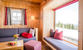 A cozy living area with wood paneling and large windows. On the table, there are fruits and flowers, and there are comfortable seating options.