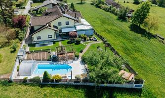 A generous property with several houses and a blue swimming pool. The garden is green and well-kept, surrounded by meadows and trees.