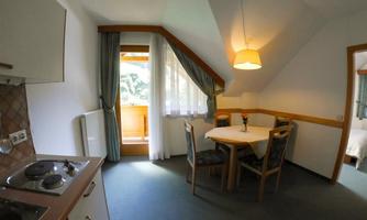 A cozy kitchen with a dining table and chairs. The room has large windows and a balcony overlooking the outdoors.
