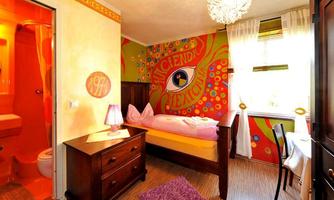 A colorfully designed room with a bed, a table, and a dresser. The walls are artistically painted and there is a private bathroom.