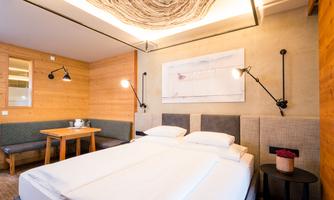 A modern bedroom with a large double bed and a unique ceiling lamp. Stylish lamps hang on the wall, and there is a dining area with a table.