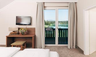 A cozy hotel room with a double bed and a desk. The windows offer a beautiful view of the lake and the surrounding nature.