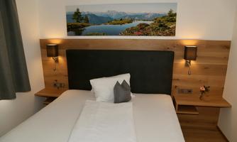 A cozy bedroom with a double bed and modern wooden furniture. A picture of a landscape with mountains and a lake hangs on the wall.