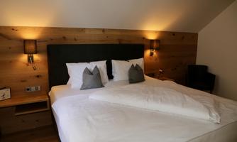 A cozy bedroom with a large double bed and warm wooden interior. The soft lighting creates an inviting atmosphere.