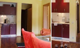 A modern kitchen with red cabinets and a brown floor. In the foreground, there is a cozy living area with a red sofa.