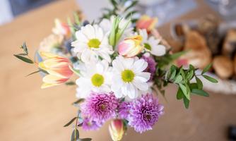 A colorful bouquet with white daisies, yellow and pink tulips, as well as purple chrysanthemums. The flowers are arranged on a table.
