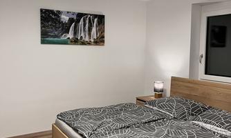 A cozy bedroom with a double bed and modern textiles. A picture of a waterfall hangs on the wall.