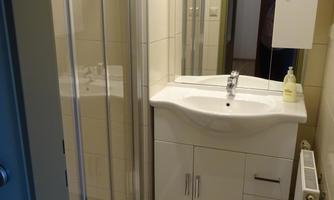 A modern bathroom with a shower cabin and a sink. It has light tiles and a clean, minimalist design.