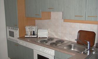 A modern kitchen with bright cabinets and a tiled cooking area. The appliances include a kettle, a microwave, and a sink.