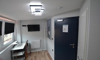 A modern room with a large window, a desk, and a television mounted on the wall. The walls are painted light, and the lighting is stylish.