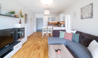 A modern kitchen-living room with an open living area. The space is bright and friendly, with a cozy sofa and a dining table.