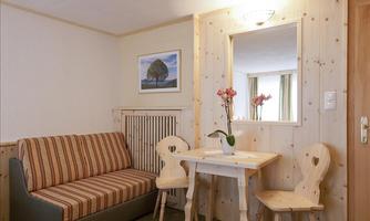 A cozy room with a striped sofa and a small table with two chairs. A picture hangs on the wall and a plant stands on the table.