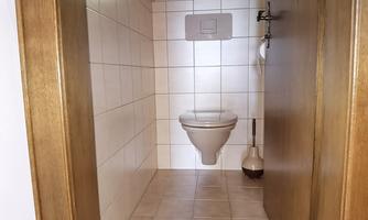 A simple bathroom area with a toilet and bright tiles. There is a small window that lets light in.