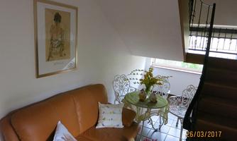 A cozy living area with a brown sofa and a small table group. Fresh flowers are on the table, and in the background, a staircase can be seen.