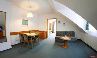 A bright room with a cozy seating area and a dining table. The sloped ceilings and the light create an inviting atmosphere.