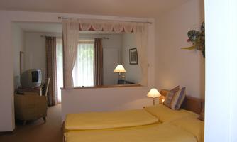 A cozy bedroom with two separate beds and yellow bedding. In the background, a living area with a television and an armchair is visible.
