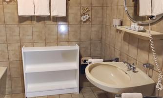 A bathroom with bright tiles, a sink, and a mirror. Towels hang on the wall and a shelf stands in the room.