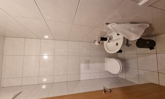 A small, modern bathroom with white tiles. There is a toilet, a sink, and a towel.