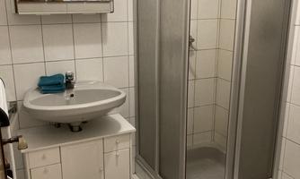 A small bathroom with a shower, a sink, and a toilet. Tiles in white and a few towels complement the space.