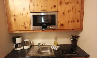 A small wooden kitchen with modern appliances. It is well-equipped with a sink, microwave, and coffee maker.
