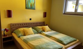A bright bedroom with yellow walls. There is a double bed with colorful bedding and two wall lamps.