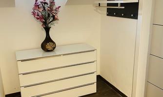 A bright hallway with a white dresser and a black wall design. A vase with colorful flowers sits on the dresser.