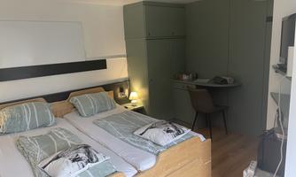 A modern bedroom with two beds and minimalist furnishings. A table and a chair complement the space, which is decorated in soft colors.