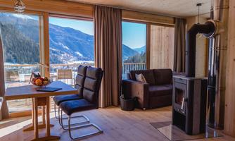 A cozy living space with a large window that offers a view of the mountains. A table, a sofa, and a fireplace create an inviting atmosphere.