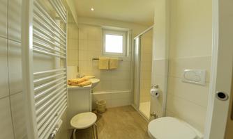 A modern bathroom with a shower, toilet, and sink. Bright tiles and towels create a friendly atmosphere.