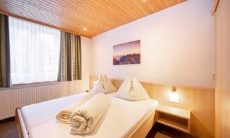 A cozy bedroom with two beds and a warm wooden ceiling. Soft lighting and a picture on the wall create an inviting atmosphere.