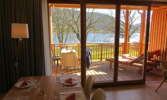 A cozy living area with a dining table and a view of a terrace by the water. Outside, the colors of spring are visible and there is a relaxing view of nature.