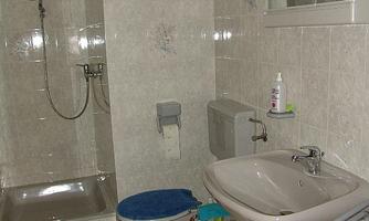 A bathroom with a shower, a sink, and a toilet. The walls are brightly tiled and there are blue bath mats.