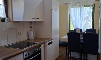 A modern kitchen with wooden countertops and white cabinets. Next to the kitchen is a dining area with a table and blue chairs.