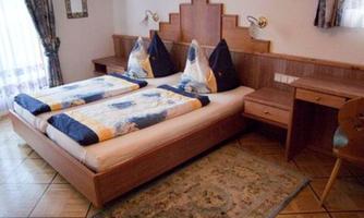 A cozy bedroom with two beds and decorative pillows. The room has wood paneling and a small desk.