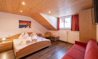 A cozy bedroom with a double bed and a red sofa.  
Large windows provide plenty of daylight and a warm atmosphere.